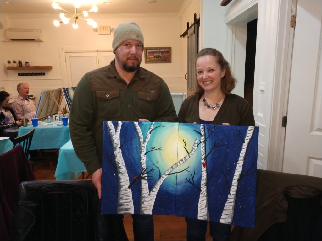 Couple holding painting created at craft class during Hearts Afire Weekend